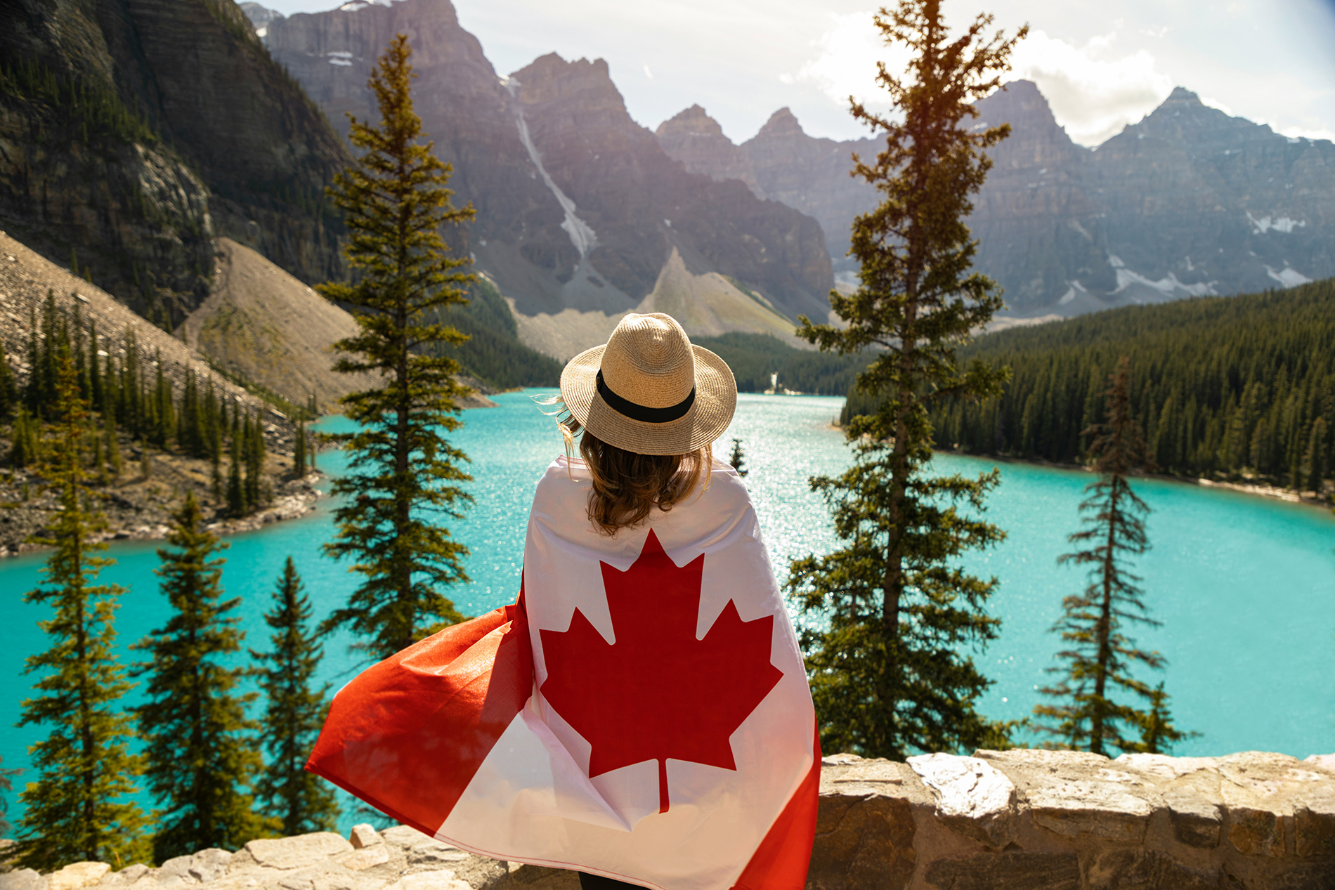 A tourist seen from behind, wrapped in a Canadian flag, admiring Moraine Lake in the Rockies—an inspiring image to help you prepare for your trip to Canada.